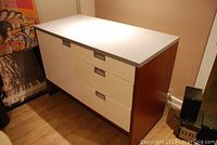 View of the cabinet from the front left side showing the white top, three drawers on the right side and one door on the left side.