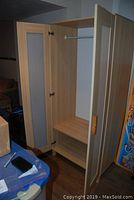 Open wardrobe cabinet showing interior hanging rod, shelf, and bottom storage compartment.
