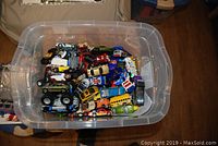 Top-down view into plastic bin filled with assorted toy cars of various makes and models.