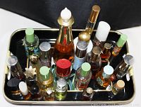 Photo showing decorated black tray with gold edges containing an assortment of vintage perfume and cologne bottles assembled upright, bottles have different colored caps and sizes.