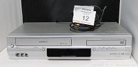 Front view of Toshiba DVD and VHS combo unit with cables and lot tag showing number 12. Shows DVD tray, VHS slot, front AV ports, buttons, and digital display panel.