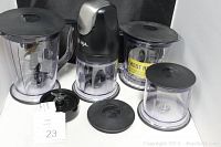 Photo showing the Ninja blender motor base, four plastic containers in various sizes with black lids, blade attachments, and white power adapter, on a white surface with black cloth background.