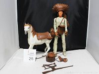 Photo showing Tonto action figure with feathered headdress standing next to white horse figure with saddle along with brown accessories on the floor.