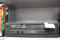 Front view of the black Technics SU-V95 integrated amplifier showing control knobs, buttons, input selector, tape monitor and volume meters, with a paper note on top right.