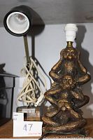 Photo shows two lamps on a shelf. One is a bronze-colored lamp with three stacked monkeys depicting 'See No Evil, Hear No Evil, Speak No Evil.' Next to it is a black lamp with an adjustable arm and white bulb socket.