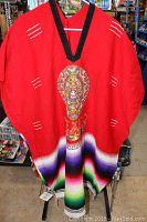 Front view of an authentic red Mexican poncho with black V-neck trim, detailed embroidery on chest, and colorful striped woven bottom.
