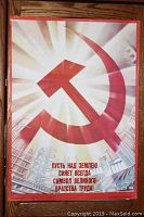 Full view of the 1980s original Soviet poster showing prominent hammer and sickle symbol with Russian text and industrial cityscape.