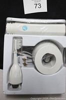 White Sonicare electronic toothbrush handle sealed in plastic, single brush head attached, round charging base, power cord, all housed in white molded plastic packaging.