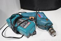 Mikita corded impact drill lying next to its charger, both with visible cords and signs of use.