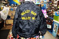 Photo of the back of the black jacket displaying the yellow embroidered text 'VALLEY BAR VALLEY Wi'
