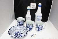 Photo of full Dutch windmills themed lot including two milk glass bottles with lids, blue and white braided floral ceramic bowl, three Williams Sonoma floral mugs, and ceramic Dutch clog shoe miniature.