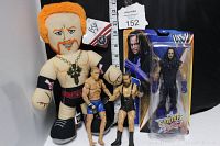 Photo shows four wrestling collectibles: one orange-haired plush wrestler doll, two loose male wrestler action figures, and one unopened The Undertaker action figure in SummerSlam packaging.