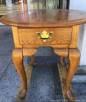 Front view of vintage oak round top table showing drawer with metal handle and curved legs