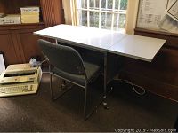 Desk and chair positioned near window, showing desk in folded state with chair placed in front