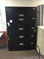 Front view of the black 5-drawer lateral file cabinet with flipper door at the top showing handles and some surface wear.