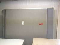 Front-facing image of a single cubicle wall panel, grey fabric with metal framing, labeled with auction tag and red tape.