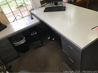 Photo of main desk with light laminate surface, drawers on the left, and computer keyboard on top. Visible wear includes scratches and tape residue.