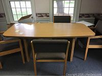 Full view of rectangular wood grain laminate conference table with 4 cushioned wood chairs around it.