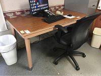 Full view of rectangular desk with woodgrain top, metal legs, and office chair underneath. Shows overall size and condition of desk.