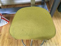 Close-up of cushioned fabric seat showing textured yellow-green upholstery with visible soiling and stains on seat surface