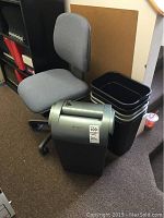 Overview of entire lot showing grey office chair, GBC paper shredder, and six black plastic wastebaskets stacked.