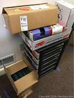 Photo showing boxes containing different sizes of plastic binding combs stacked on and next to a 6-drawer black plastic storage unit.