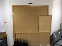 Three cork boards visible, largest positioned behind the smaller two leaning against a wall and chairs nearby.