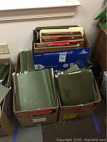 Three boxes of hanging file folders, two with predominantly green folders and one box labeled Staples multipurpose paper box with mixed folders.