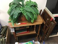 Wood bookshelf table with faux fern in copper kettle vase on top and wood folding table beside it.