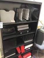 Wide view of black metal shelving unit containing document organizers, file racks, plastic trays, and 3-ring binders.