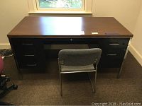 Front view of woodgrain top metal desk with gray fabric and metal chair positioned in front.