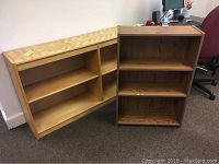 Two wooden bookshelves side by side, one light wood with loose backing nails, the other darker wood with visible surface damage.