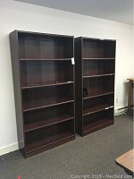 Two dark wood bookcases standing side by side against a white wall, showing full height and width.