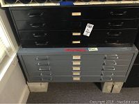 Photo showing stacked black 4-drawer flat file on top of gray 5-drawer flat file, both metal with label holders on each drawer, on concrete blocks.