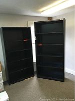 Two black metal bookshelves standing next to each other in a room, both with multiple shelves.
