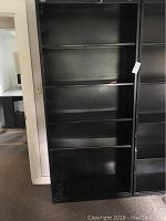 Front view of one black metal bookshelf showing five shelves and solid back panel