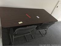 Top view of rectangular folding table and two gray folding chairs stored underneath