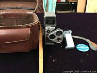 Photo showing the leather carrying case open with the movie camera, grip, and photographer pin on display.