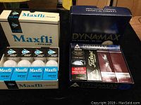 Photo showing two boxes of golf balls side by side: one Maxfli by Dunlop box containing four small boxes of three balls each, and one DynaMax box with assorted golf balls inside.