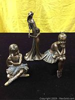 Three vintage figurines displayed against yellow background and black surface.