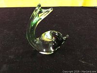 Angled side view of the clear glass fish figurine showing upward curved tail and head on black cloth background with yellow backdrop.