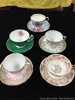 Five bone china cups and saucers arranged on black cloth, showing various floral patterns and gold trim
