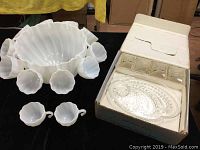 Wide view of milk glass punch bowl with 12 matching cups arranged around it, next to boxed 4-piece clear glass snack set.