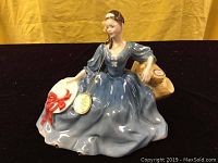 Front view of the Royal Doulton Elyse figurine showing the blue dress, white hat with red ribbon, and original paper tag attached by gold string.