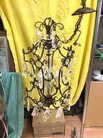 Full view of the chandelier showing six arms, hanging clear crystal pendants and three candle-style light bulbs. Metal chain and canopy are visible.