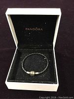 Black braided leather bracelet with silver clasp inside black velvet interior with Pandora logo