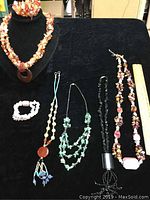 Full lot arranged on black fabric with black jewelry bust, showing 5 necklaces including multi-strand chip stone and pendant necklaces, 1 matching bracelet on bust, and 1 pink quartz bead bracelet