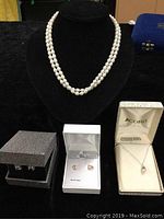 Two-strand cultured pearl necklace displayed on black bust with three sets of earrings in boxes underneath: pearl and cubic zirconia earrings visible.