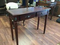 Full angled view of mahogany console table showing side and front with two drawers and tapered legs on wood floor.