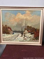 Framed oil painting of a snowy rural landscape with houses, bare trees and cloudy sky.